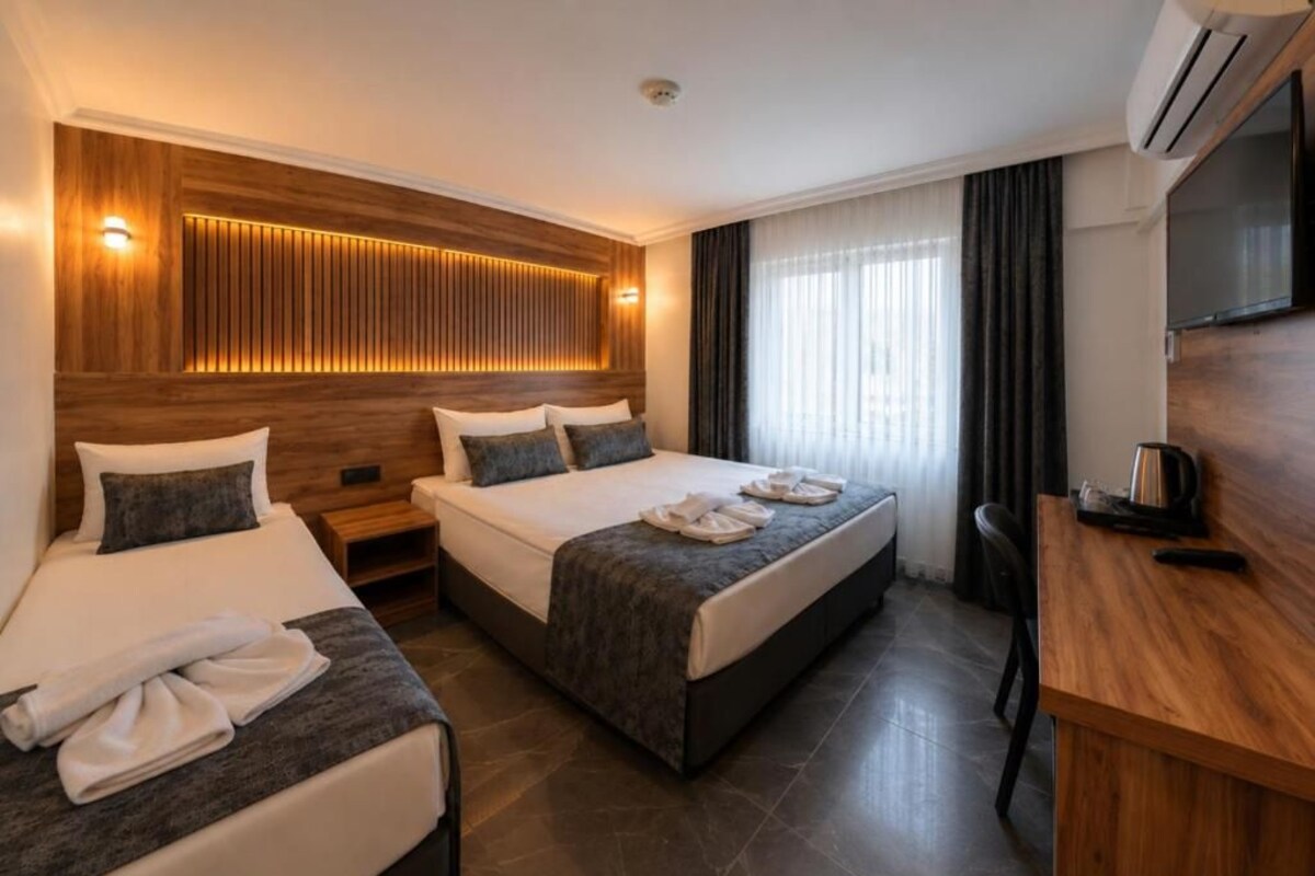Habitación de hotel con dos camas, televisión, escritorio y cabecera de madera con iluminación integrada.