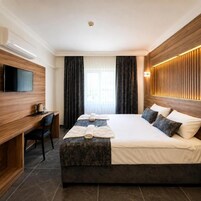 Quarto de hotel com cama, escrivaninha, televisão e luminária fixada na parede.