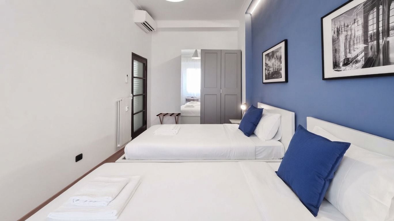 Ein Hotelzimmer mit zwei Betten, einem Heizkörper, einem Fenster und einer Tür zu einem Badezimmer.
