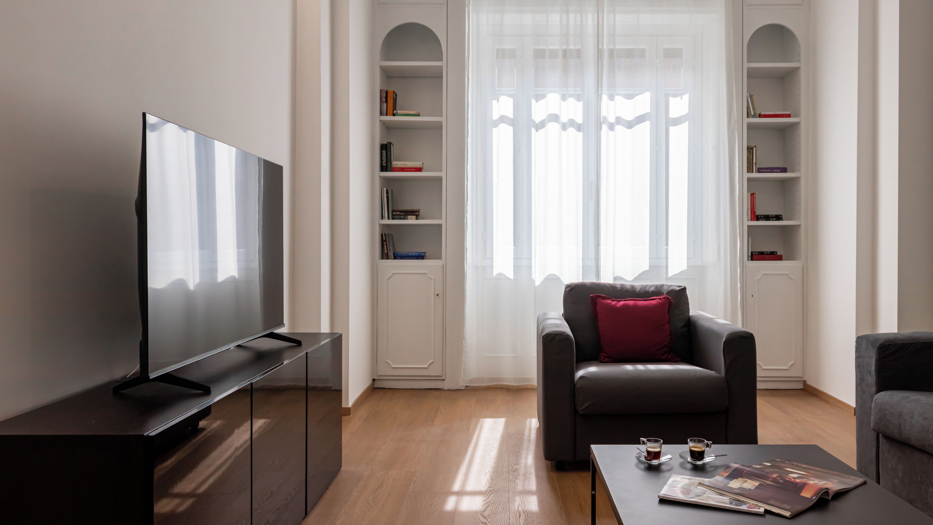 Ein modernes Wohnzimmer mit einem Flachbildfernseher, einem Ledersessel, einem Couchtisch mit einer Zeitschrift und einem Bücherregal.