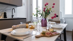 Ruokapöytä on katettu lautasilla, laseilla, maljakossa olevilla kukilla sekä puulevyllä, jonka päällä on juustoja ja leikkeleitä.