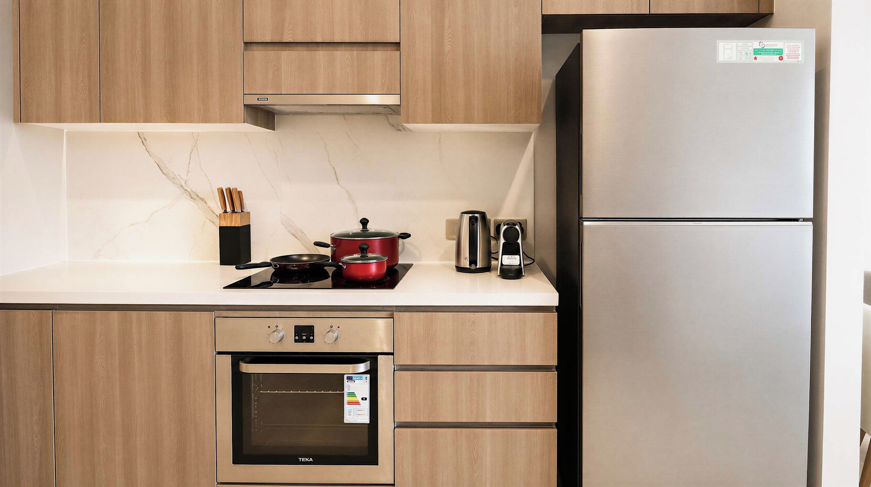 A kitchen with a built-in oven, a stovetop, a refrigerator, and a kettle.