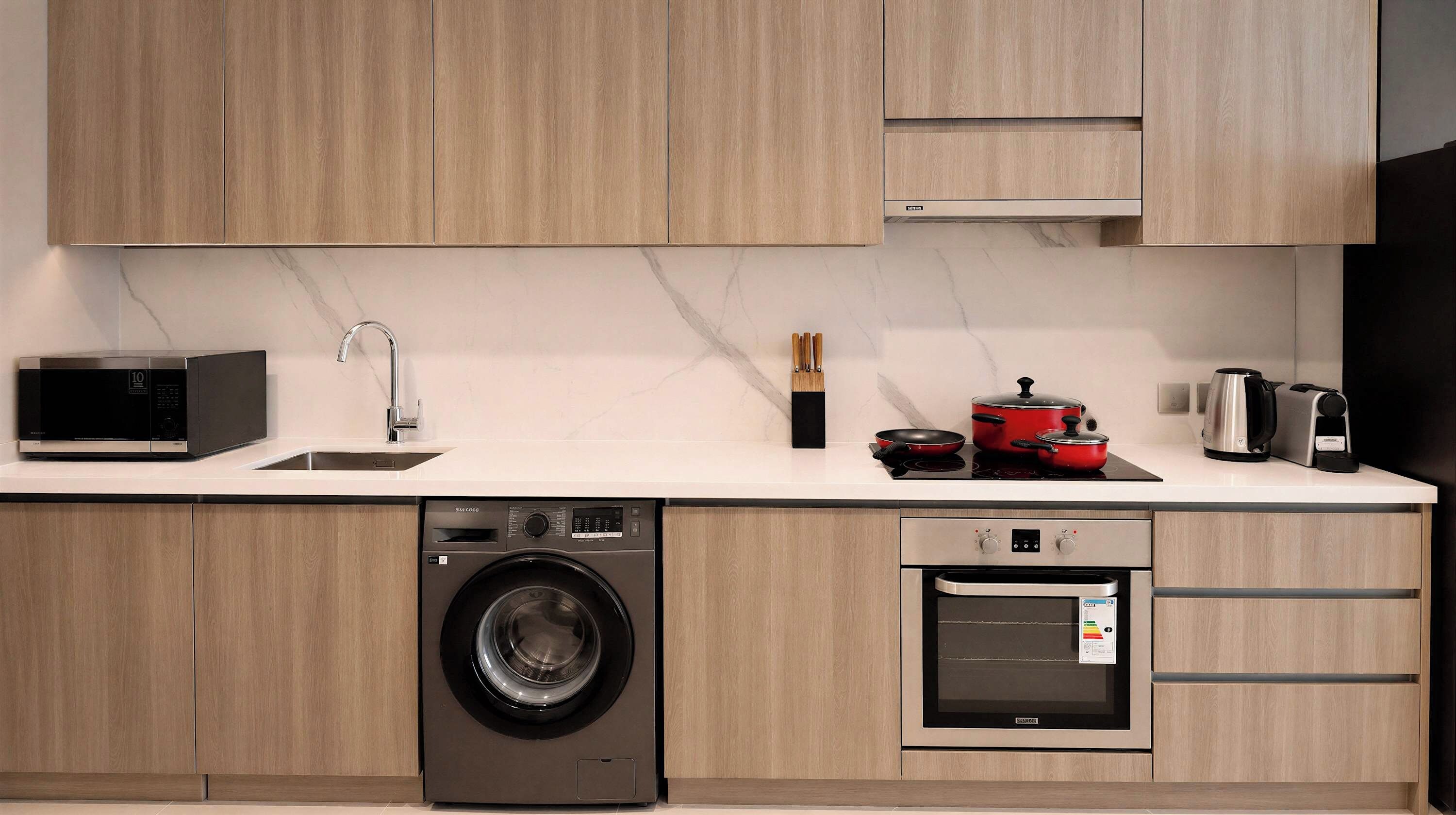 A modern kitchen with a washing machine, oven, microwave, and a coffee maker.