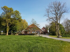 A traditional brick house with a sloped roof, surrounded by a well-maintained lawn and mature trees. - Crildumersiel Farm (Wangerland)