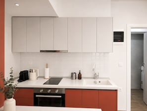 A modern kitchen with white cabinets, a black induction cooktop, a stainless steel range hood, and a built-in oven. - Quiet City Studio w/ Kitchen near Ladadika (Thessaloniki)