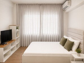 A bedroom with a bed, a TV on a stand, a bedside table, and a window with curtains. - Quiet City Studio w/ Kitchen near Ladadika (Thessaloniki)