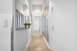 A modern hallway with white walls, wooden flooring, and artwork on the walls. There are light switches and a door at the end. - Exclusive Penthouse Apartment with Sauna and Balcony near Priwall Beach (Lübeck)
