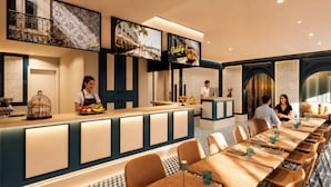 Un restaurante con una larga barra, varias zonas de estar y una pantalla de televisión que muestra un paisaje urbano.