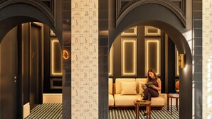 Un interior moderno con piso de diseño geométrico, una zona de estar central con sofá y sillones, y un gran panel decorativo con ilustraciones.