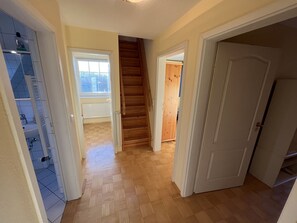 A hallway with a wooden staircase, a white door, and a view of a window. - Dünenzauber – Your Relaxing Getaway at Schönberger Strand (Schönberg (Holstein))