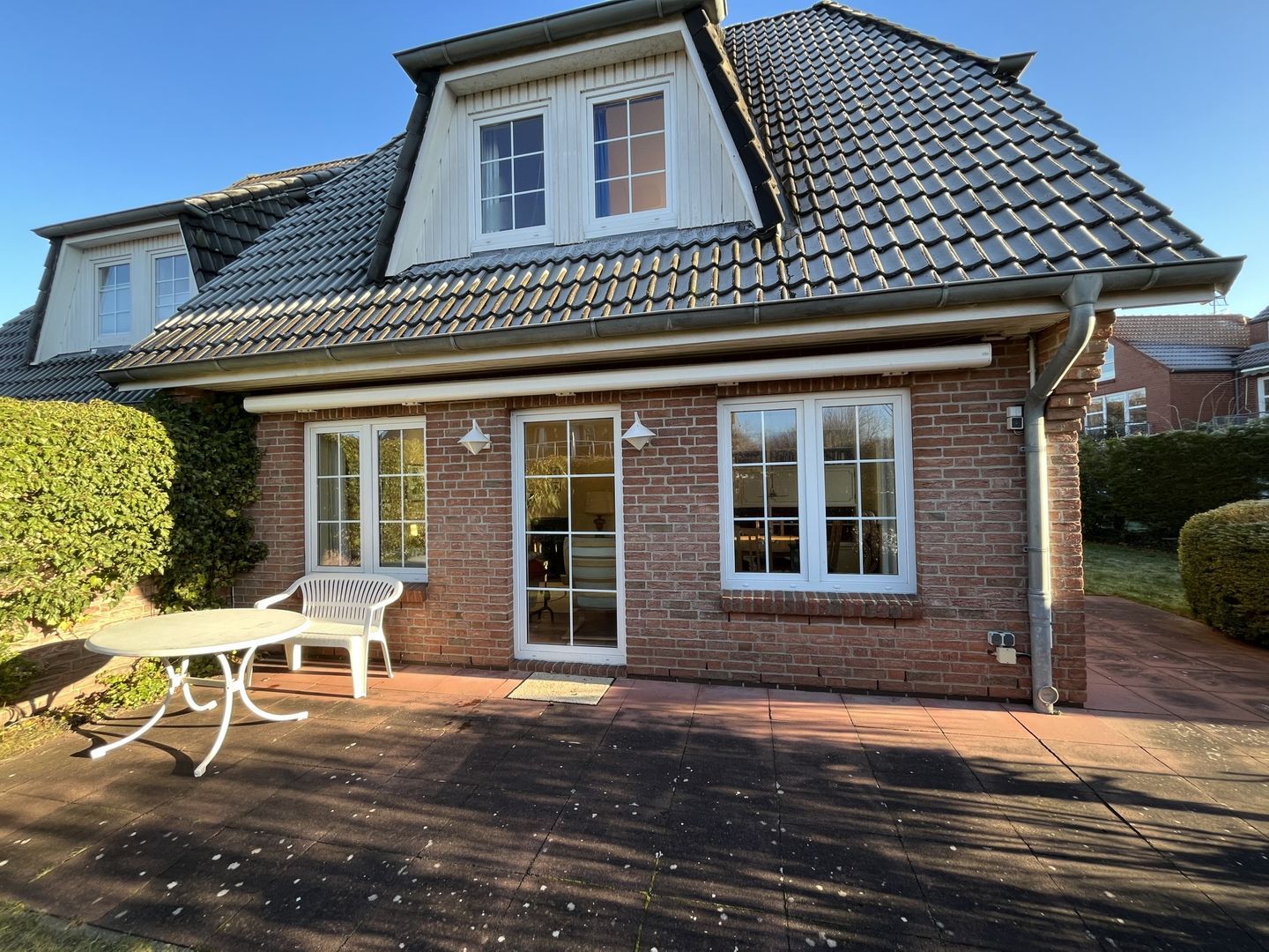 Une maison à deux étages, avec une façade en briques, des fenêtres à cadre blanc et un toit recouvert de tuiles.