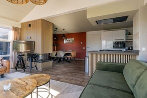 A modern kitchen with a built-in oven, a dining area with a table and chairs, and a living room with a green sofa and a wooden coffee table. - Holiday home with 3 bedrooms (Oude-Tonge)