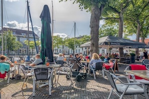 An outdoor café with tables and chairs, a stroller, and umbrellas. - Holiday home with 3 bedrooms (Oude-Tonge)