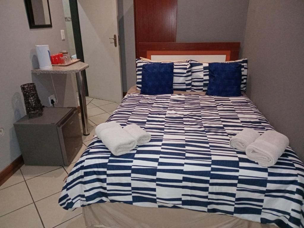 Una habitación de hotel con edredón a cuadros, dos almohadas, una mesita de noche con lámpara y un pequeño armario.