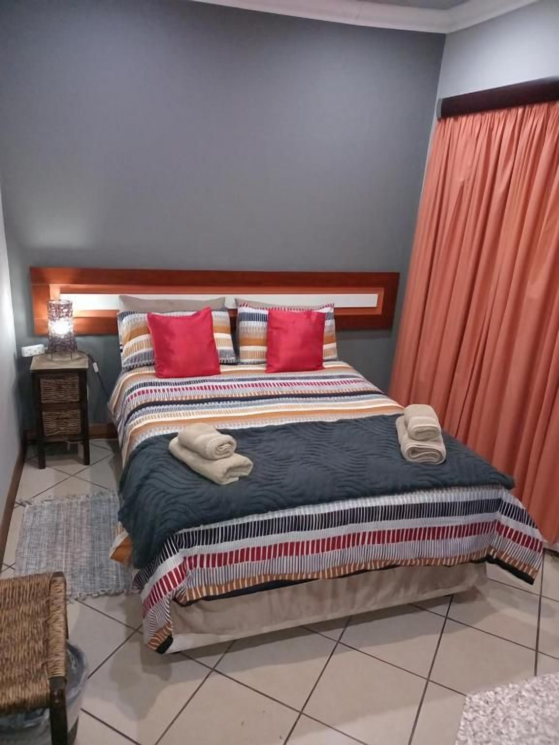 Un letto rifatto con uno s sopra coperta a righe e due cuscini, un comodino con una lampada e una finestra con tende.