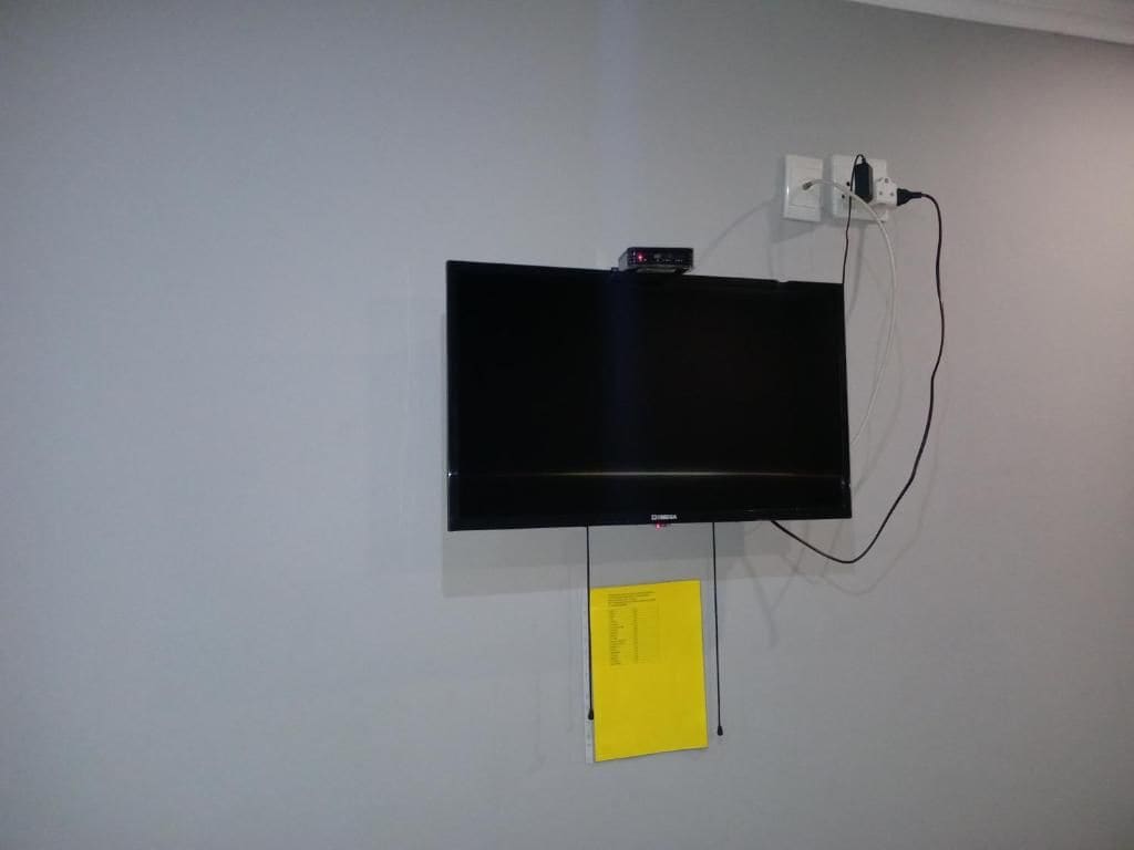 A flat-screen TV mounted on a plain wall with a power cord and a yellow note attached below.