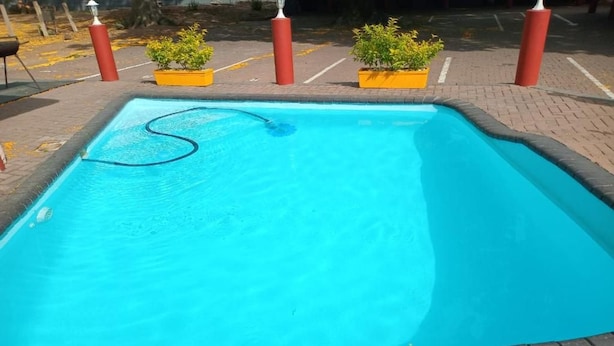A rectangular swimming pool with a clear blue water surface, surrounded by a brick border. - Grand Central Guesthouse (Rustenburg)
