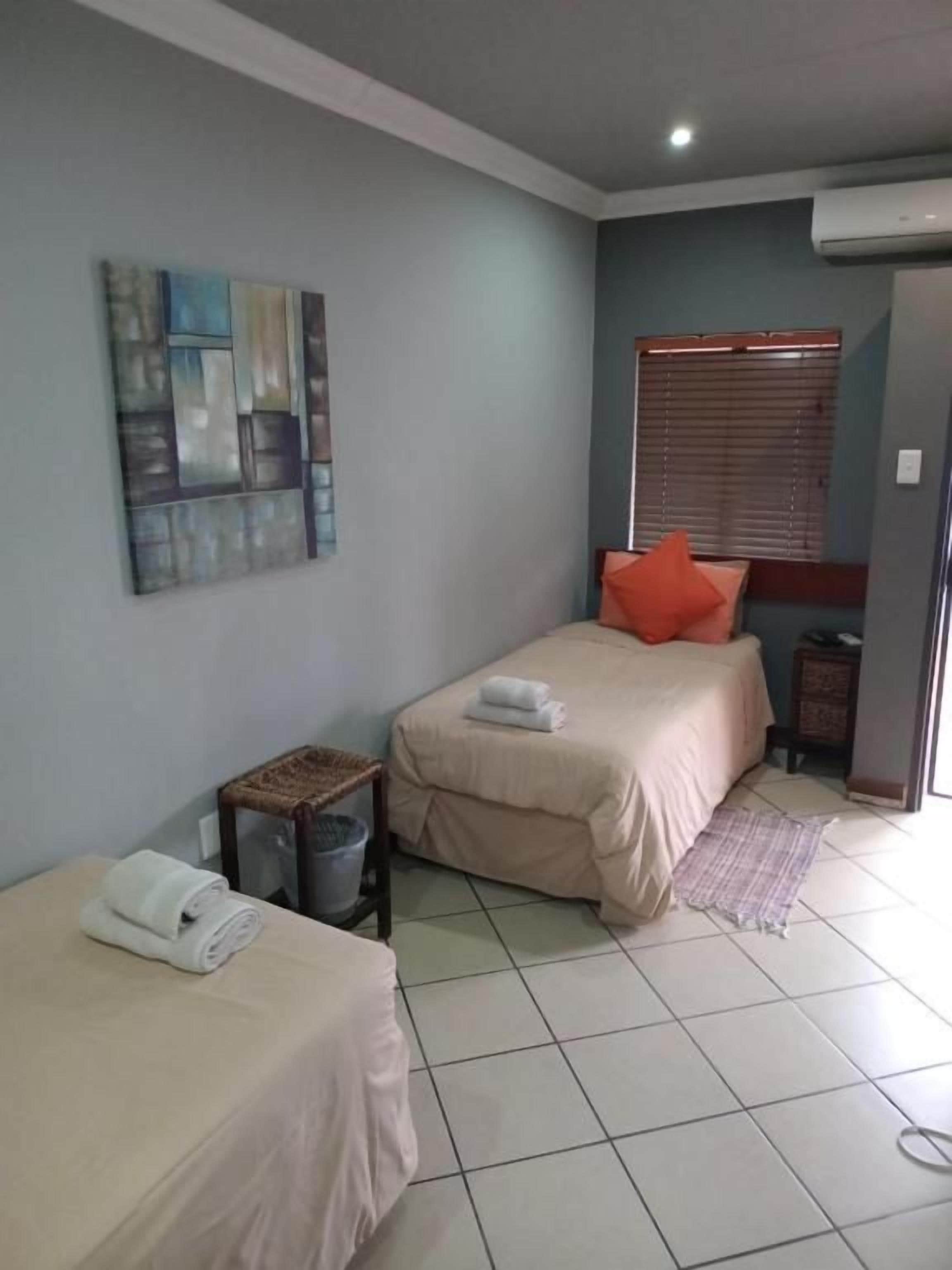 A bedroom with two beds, a window with blinds, a wall-mounted air conditioner, and a small table with a basket.