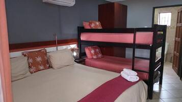 Una cama litera con colcha roja y color crema, cabecera de madera y toalla roja en el reposapiés.