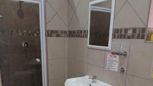 A bathroom with a shower, sink, toilet, and a notice on the wall. - Grand Central Guesthouse (Rustenburg)
