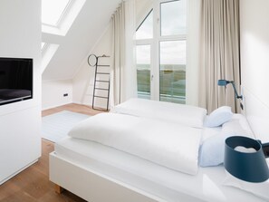 A modern bedroom with a bed, a TV, a window, and a view of the outdoors. - Meer.loft.juist.9 (Juist)