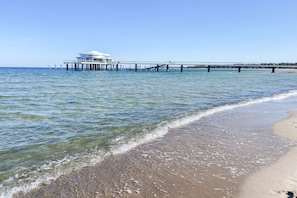 Ein Strand mit einem Steg, der sich ins Wasser erstreckt, ein Gebäude auf dem Steg und ein klarer Himmel.