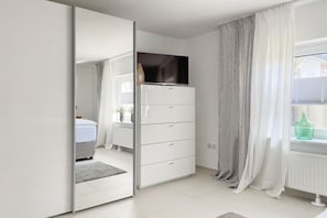 Ein modernes Schlafzimmer mit Kleiderschrank, Bett und einem Fenster mit Vorhängen.