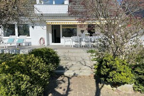 Ein Gebäude mit überdachter Außenbestuhlung, Stufen zum Eingang und einem Pool im Hintergrund.