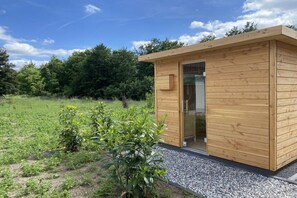 Eine kleine Holzhütte mit Glastür, umgeben von einem Kiesweg und Grünpflanzen.