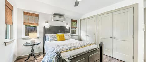 A bedroom with a bed, bedside table, lamp, air conditioning unit, ceiling fan, and wardrobe.