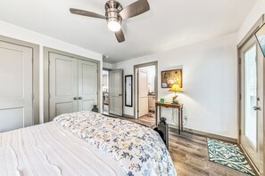 Ein Schlafzimmer mit einem Bett, einem Deckenventilator, einem Nachttisch, einer Lampe und einer Tür.
