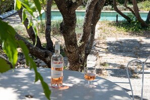 A table with a bottle of wine and a glass, set outdoors with a tree and a body of water in the background. - Holiday home in Joucas with swimming pool (Joucas)