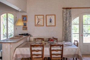 A dining area with a table set for two, framed artwork on the wall, and a window with curtains. - Holiday home in Joucas with swimming pool (Joucas)