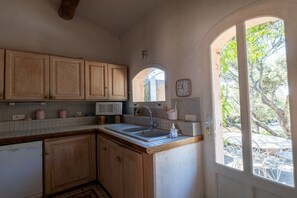 A kitchen with wooden cabinets, a microwave, a sink, and a clock on the wall. - Holiday home in Joucas with swimming pool (Joucas)
