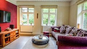 Een woonkamer met een rode muur, een houten entertainmentkast, een bank en een bijzettafeltje.