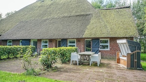 A brick house with a thatched roof, a small garden, and outdoor seating. - Haubarg Tetenshof Jägerglück: A Historic Vacation Home for a Relaxing Getaway (Welt)