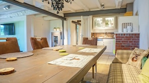 A dining area with a wooden table, chairs, and a kitchen in the background. - Haubarg Tetenshof Jägerglück: A Historic Vacation Home for a Relaxing Getaway (Welt)