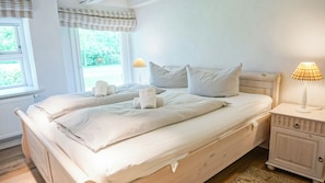 A bedroom with a bed, pillows, a bedside table with a lamp, and a window with curtains. - Haubarg Tetenshof Jägerglück: A Historic Vacation Home for a Relaxing Getaway (Welt)