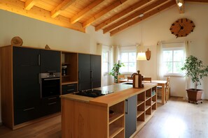A modern kitchen with a wooden ceiling, a large island, and a dining area with a table and chairs. - Haus Drischlag Vacation Rental (Ramsau bei Berchtesgaden)