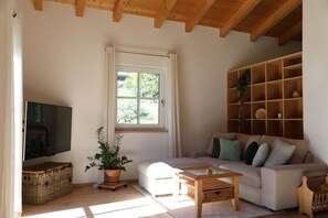 A living room with a sofa, a coffee table, a television, a window, and a wooden bookshelf. - Haus Drischlag Vacation Rental (Ramsau bei Berchtesgaden)