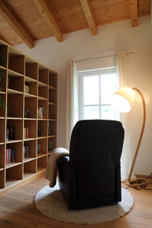 Ett rum med en svart stol, en bokhylla, ett fönster med gardiner och en golvlampa.