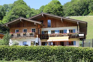 A two-story wooden chalet with balconies, surrounded by lush greenery and a hedge. - Haus Drischlag Vacation Rental (Ramsau bei Berchtesgaden)