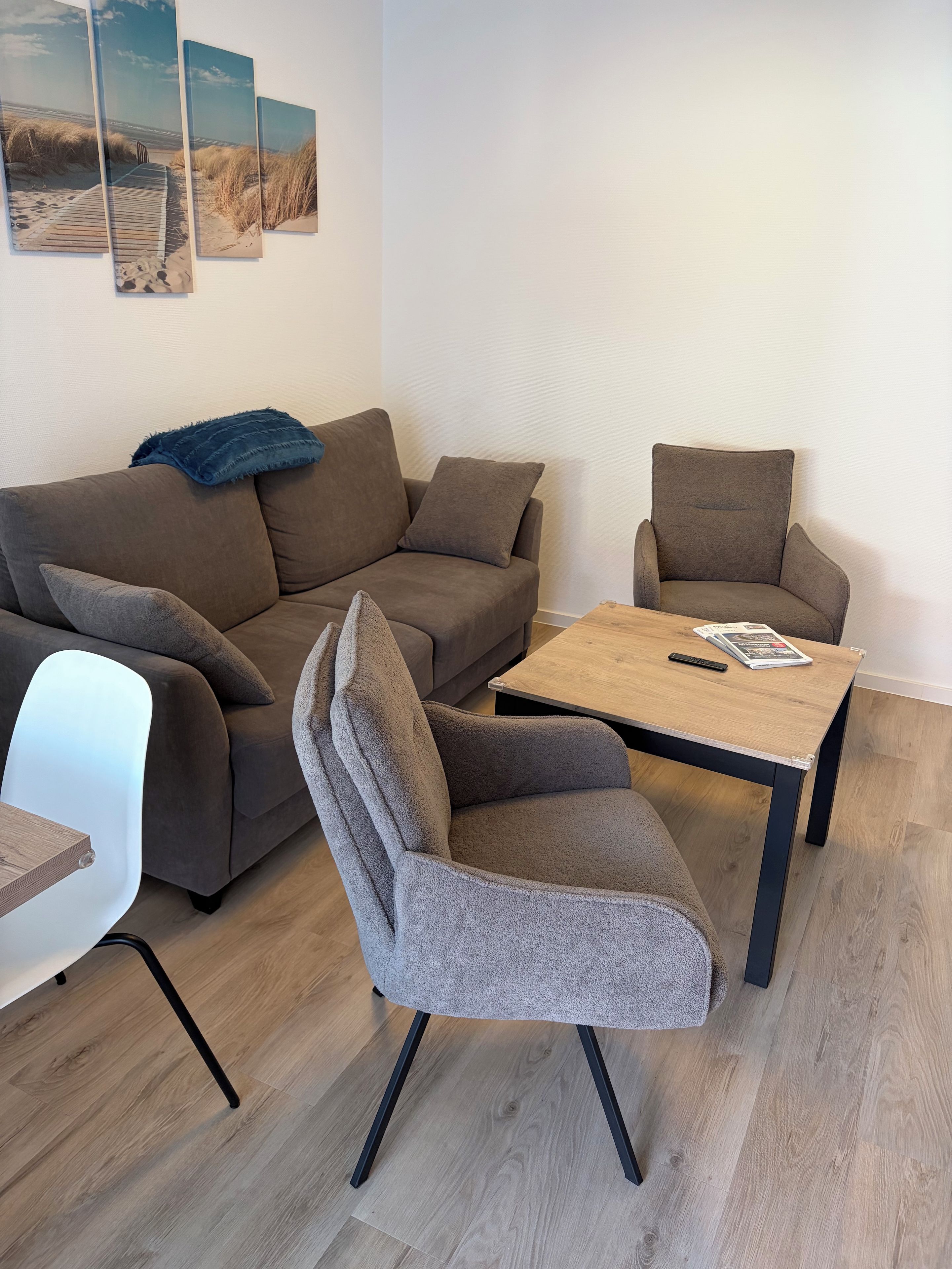 Ein modernes Wohnzimmer mit einer Couch, zwei Sesseln, einem Couchtisch und einem Beistelltisch.