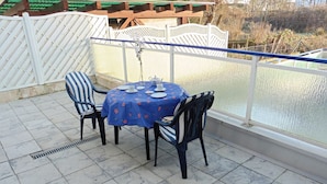 Eine Terrasse mit einem runden Tisch, gedeckt für vier Personen, umgeben von Stühlen und Blick auf ein Gewässer durch eine Glaswand.