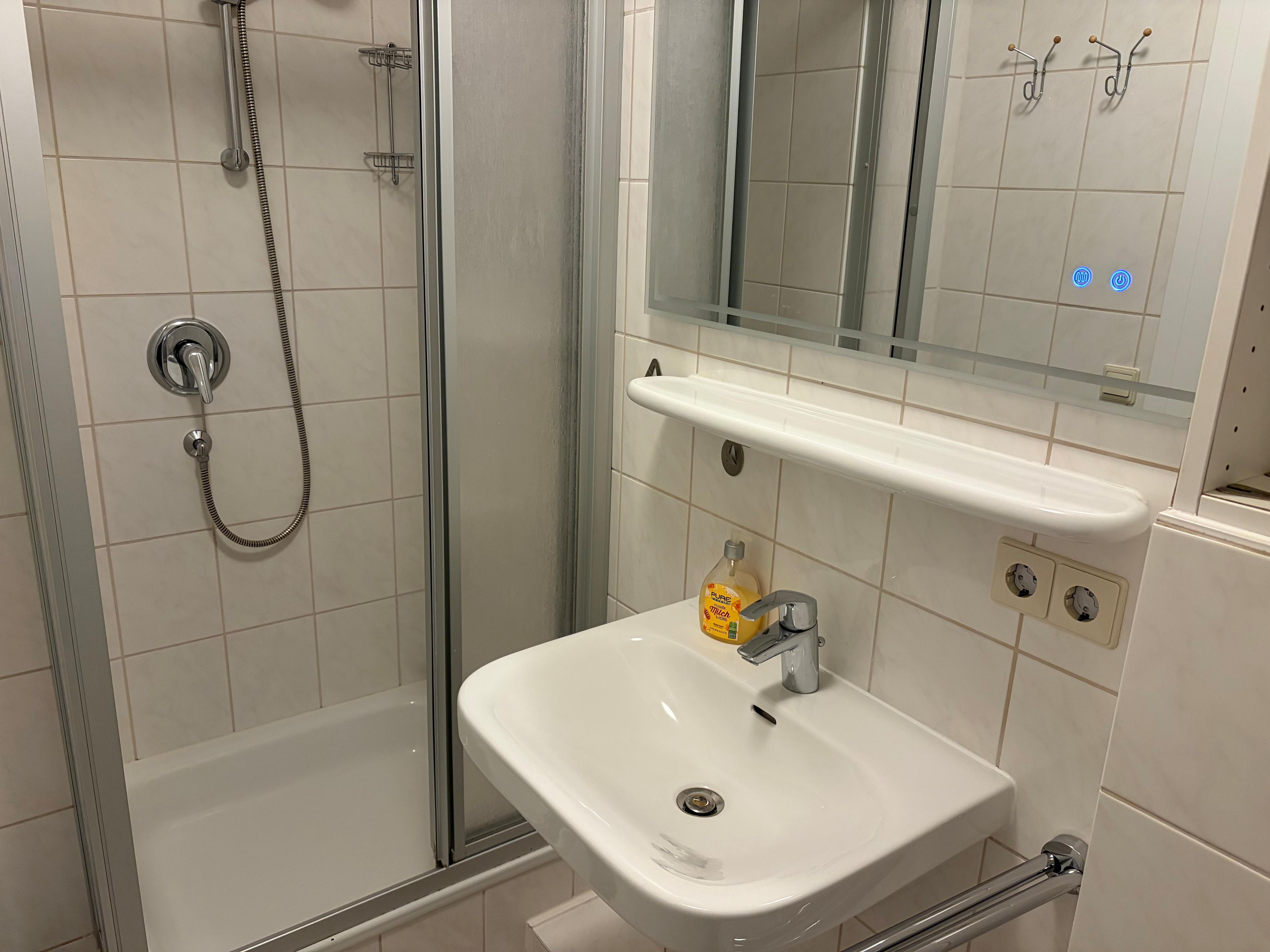 Ein Badezimmer mit einer Duschkabine, einem weißen Waschbecken und einem Spiegel darüber.