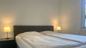 Ein Doppelbett mit Kopfteil, zwei Nachttische mit Lampen und ein Fenster mit Jalousien.