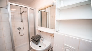 Ein Badezimmer mit einer Duschkabine, einem weißen Waschbecken und einem Spiegel darüber.