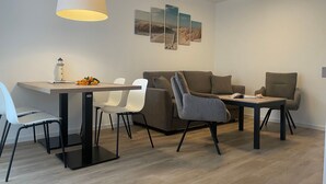 Ein modernes Wohnzimmer mit Essbereich, ausgestattet mit einer Couch, Sesseln, einem Tisch und Bildern an der Wand.