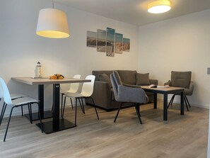 Uma sala de estar moderna com área de refeições, com sofá, cadeiras, mesa e obras de arte na parede.