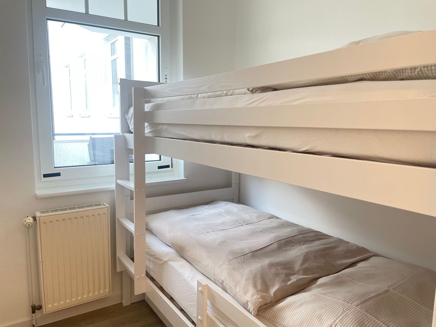 En køjeseng med et vindue over og en radiator under, samt udsigt til bygninger.
